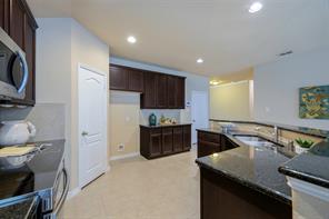 Kitchen with dark stone counters, stainless steel dishwasher, pendant lighting, light tile floors, and sink
