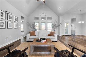 Living room featuring a stone fireplace with gas, wood-style floors, ceiling fan, and high vaulted ceiling