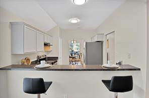 Kitchen with appliances with stainless steel finishes, vaulted ceiling, white cabinetry, dark hardwood / wood-style flooring, and sink