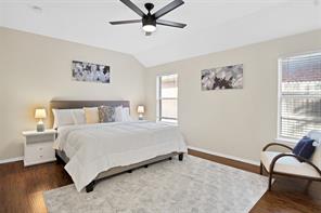 Bedroom with lofted ceiling, ensuite bath, dark wood-type flooring, and ceiling fan