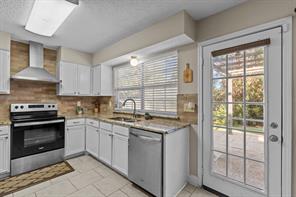 Kitchen featuring appliances with stainless steel finishes, wall chimney exhaust hood, sink, and white cabinets