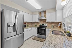 Kitchen with appliances with stainless steel finishes, tasteful backsplash, white cabinets, light stone countertops, and a textured ceiling