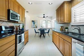 Kitchen with ceiling fan, a raised ceiling, backsplash, appliances with stainless steel finishes, and dark stone counters